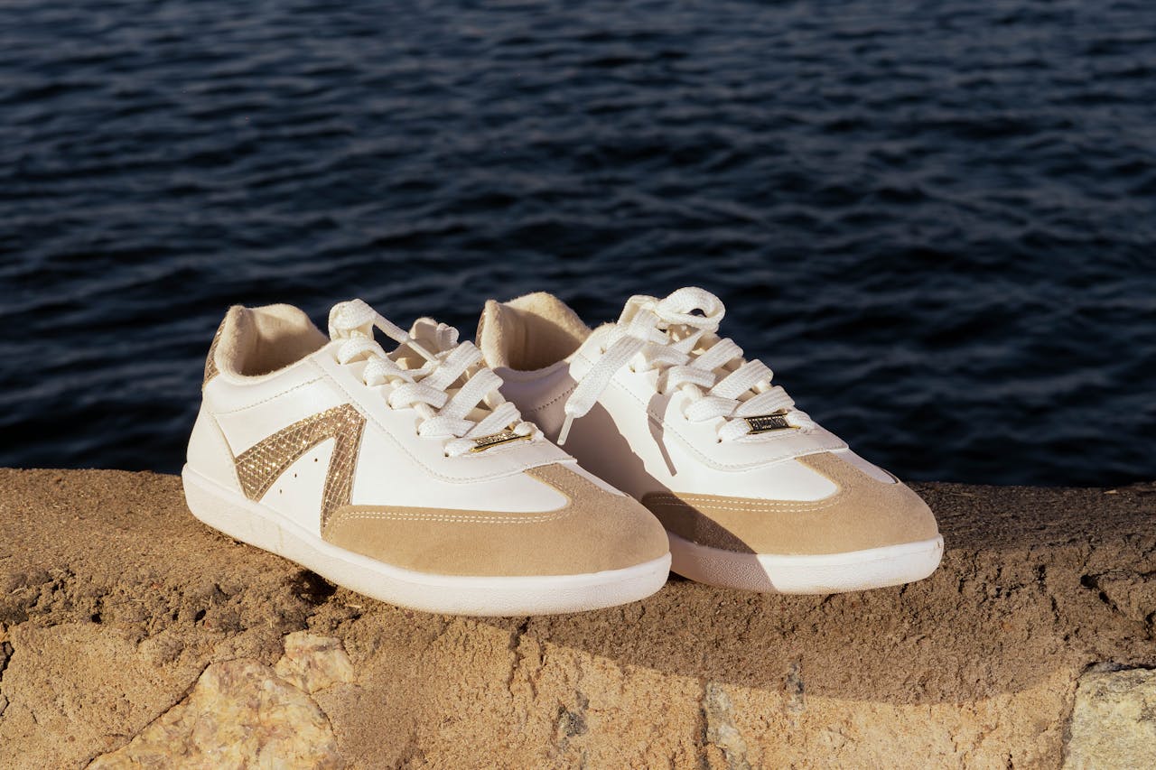 Trendy beige and white sneakers placed on a stone surface by the water, perfect for lifestyle and fashion themes.