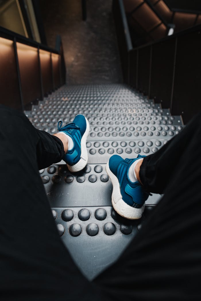 Person wearing blue sneakers and black pants sitting on metal stairs.